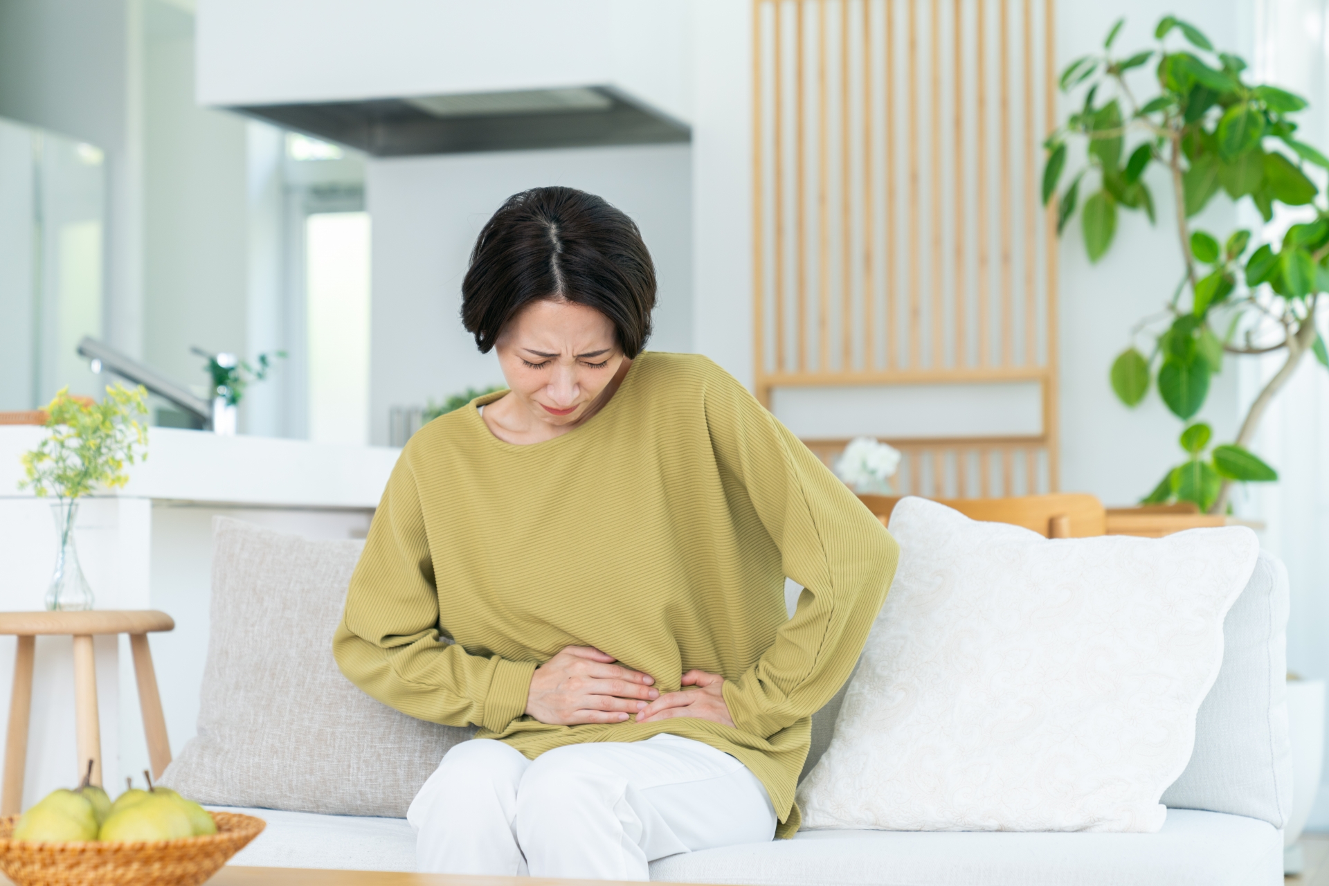 ソファに座り、腹部を押さえる女性