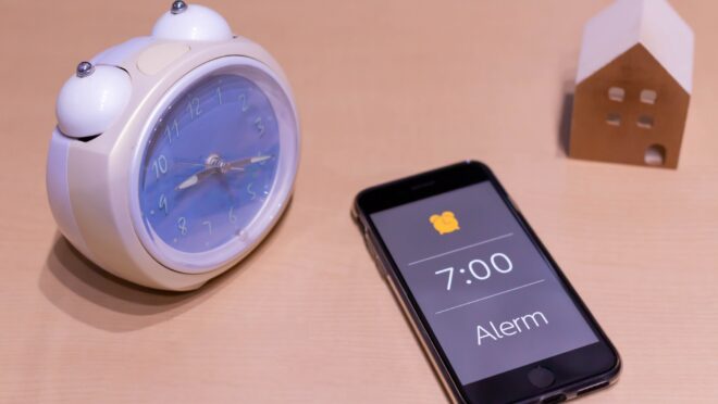 机に置かれた目覚まし時計とスマートフォン