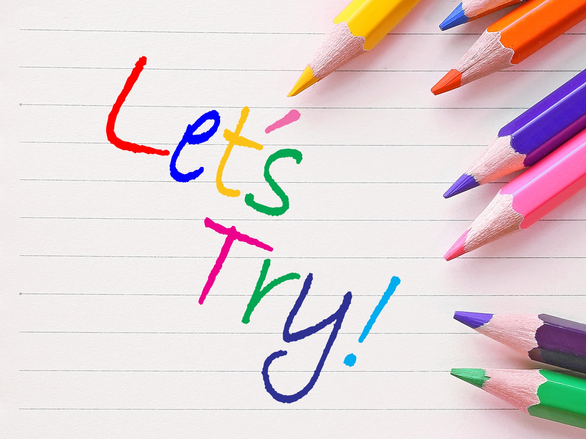 ノートの上に並んだ色鉛筆。ノートには「Let’s try！」と記載されている