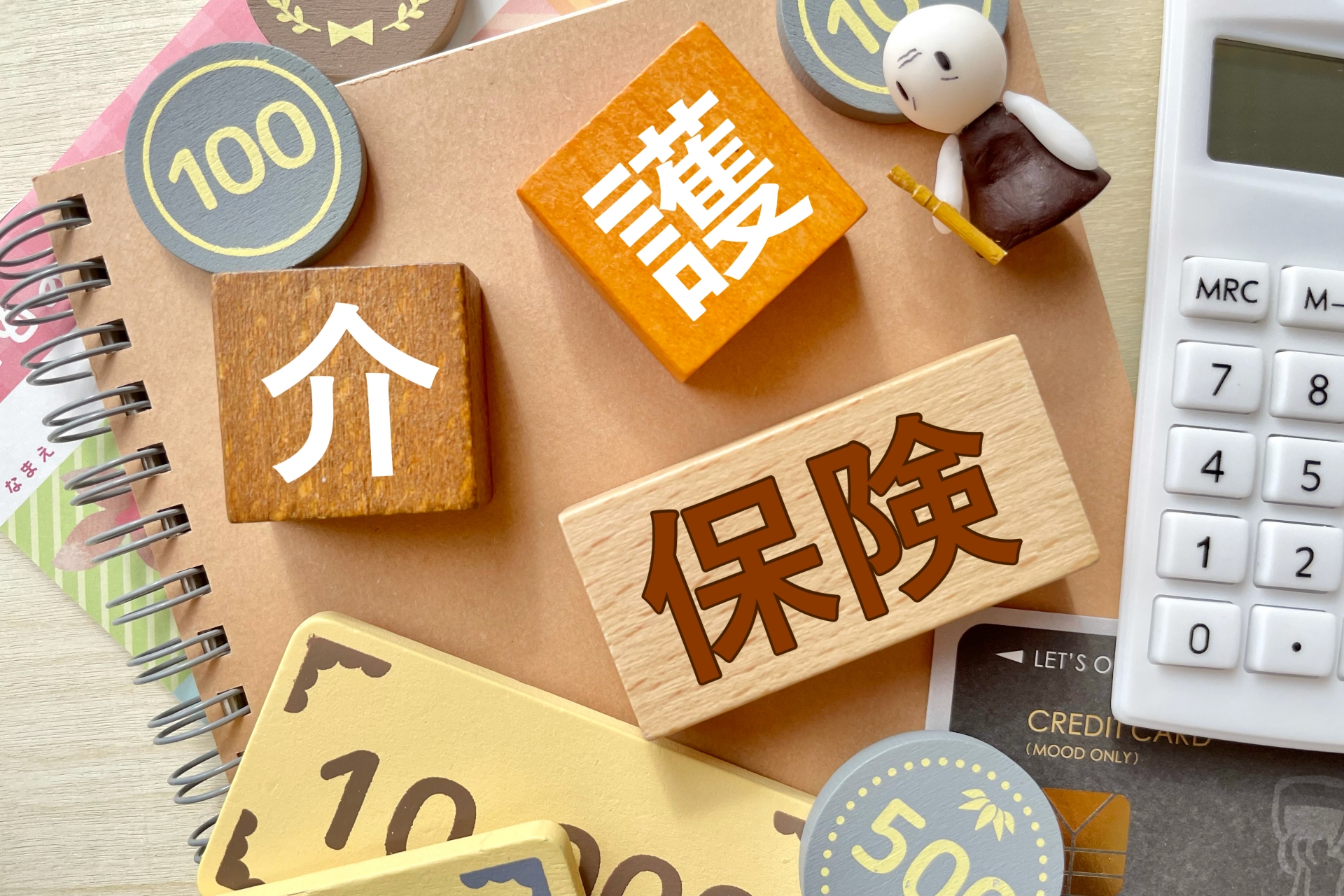 「介護保険」と記載されたブロック、お金を模した積み木、高齢者をイメージした人形が机に置かれている