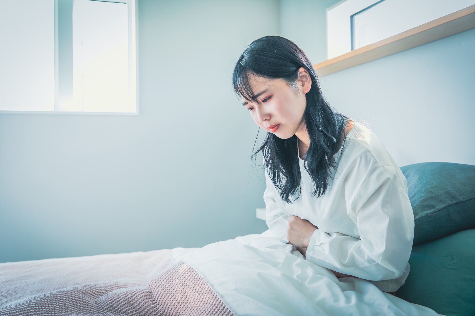 ベッドで腹部を押さえる女性