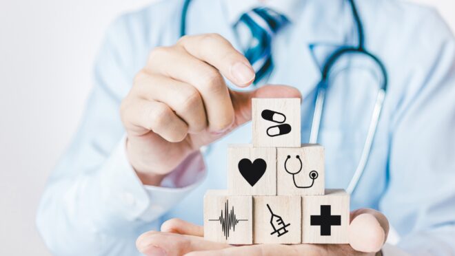 医師の手に聴診器や薬などのマークが書かれたブロックを積む様子