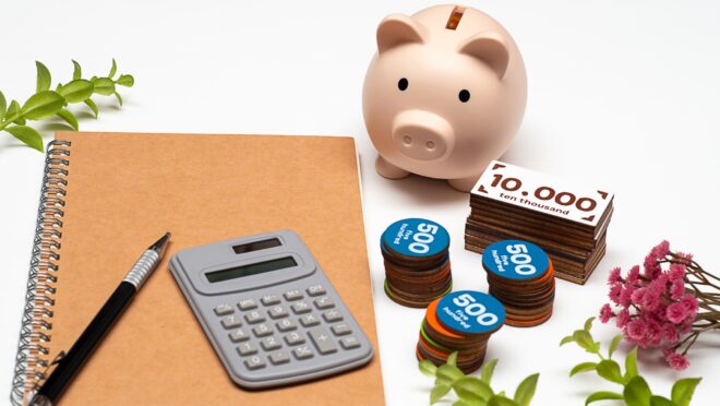 ノート、電卓、貯金箱、お金を模したブロックが机の上にある様子