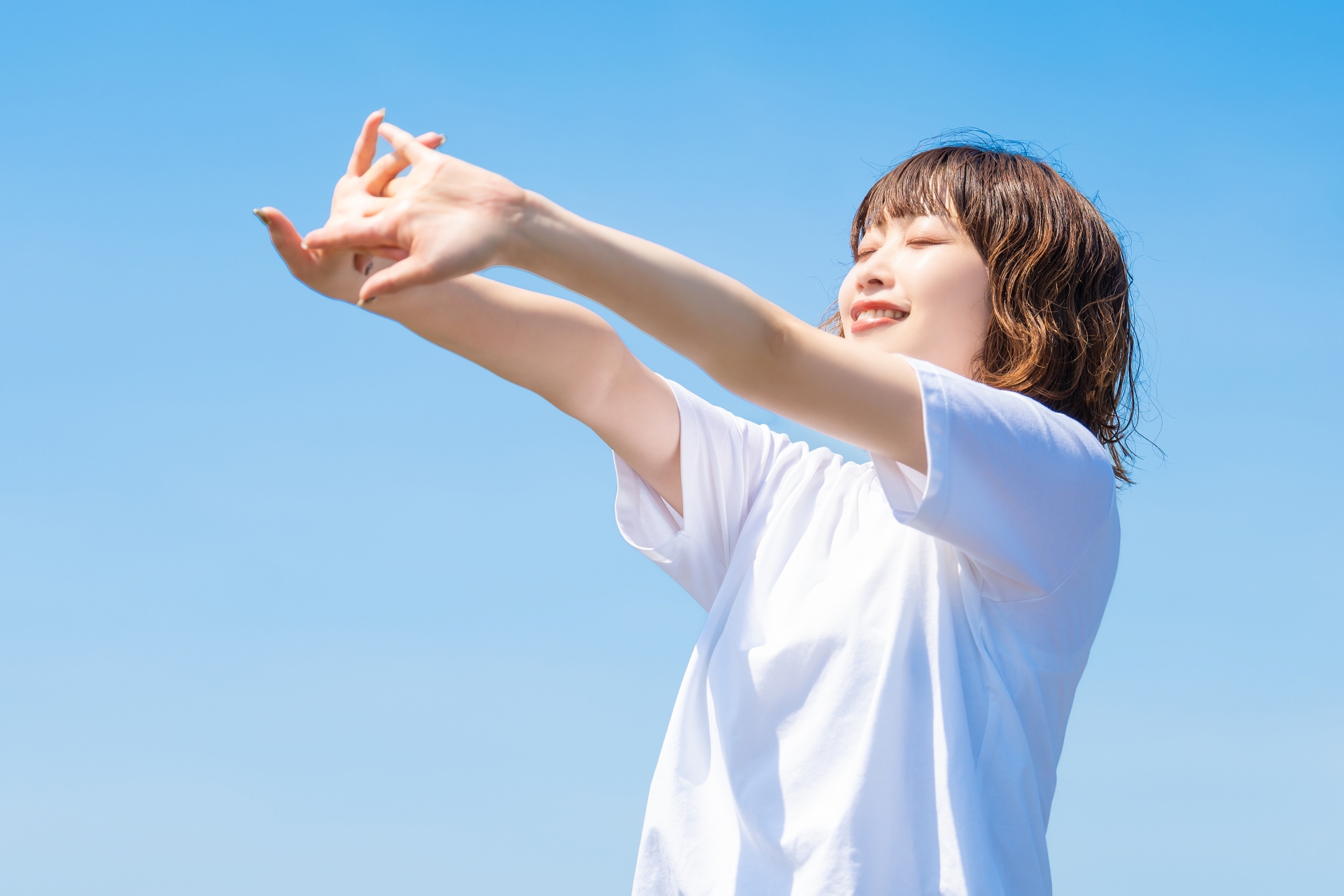 青空の下で腕を伸ばす女性