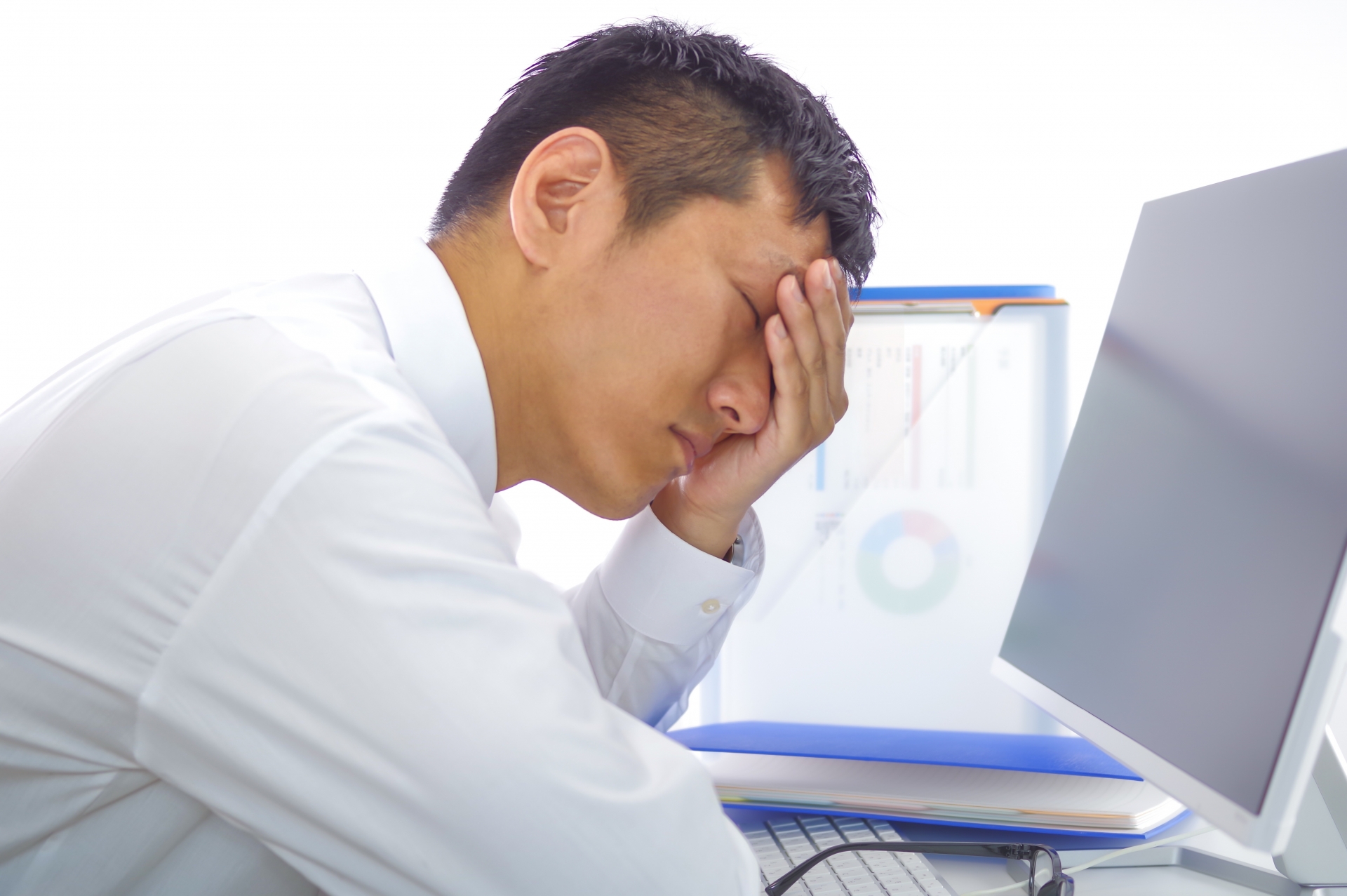 PCの前で頭を押さえる男性